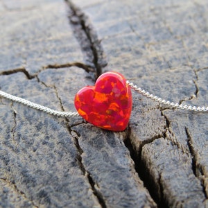May include: A silver chain necklace with a red and orange heart-shaped pendant. The pendant has a speckled, iridescent finish.
