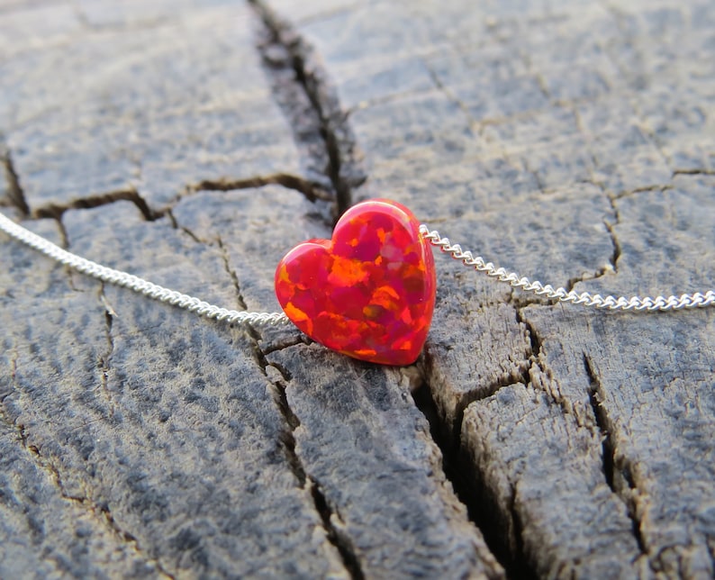 May include: A silver chain necklace with a red and orange heart-shaped pendant. The pendant has a speckled, iridescent finish.