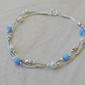 K&ouml;nnte beinhalten: Ein silbernes Armband mit drei Kettenstr&auml;ngen und blauen Opal- und wei&szlig;en Perlen.
