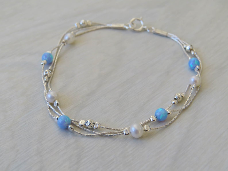 K&ouml;nnte beinhalten: Ein silbernes Armband mit drei Kettenstr&auml;ngen und blauen Opal- und wei&szlig;en Perlen.