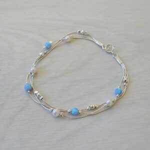 K&ouml;nnte beinhalten: Ein silbernes Armband mit mehreren Kettenstr&auml;ngen und blauen Opal- und wei&szlig;en Perlen.