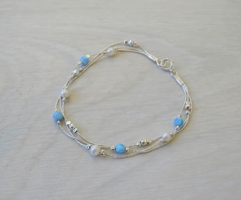 K&ouml;nnte beinhalten: Ein silbernes Armband mit mehreren Kettenstr&auml;ngen und blauen Opal- und wei&szlig;en Perlen.