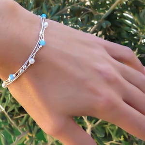 K&ouml;nnte beinhalten: Ein silbernes Armband mit mehreren Str&auml;ngen und blauen und wei&szlig;en Perlen. Das Armband befindet sich an einem Handgelenk.