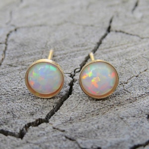 Puede incluir: Un par de pendientes de oro con piedras de &oacute;palo blanco. Los pendientes est&aacute;n engastados en un dise&ntilde;o redondo simple.