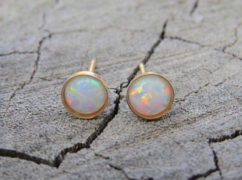 Puede incluir: Un par de pendientes de oro con piedras de &oacute;palo blanco. Los pendientes est&aacute;n engastados en un dise&ntilde;o redondo simple.