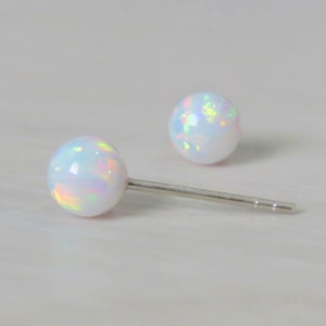 Pode incluir: Um par de brincos de prata com pedras de opala branca. As pedras têm um brilho iridescente arco-íris.