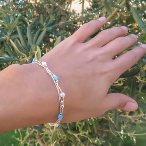 K&ouml;nnte beinhalten: Ein silbernes Armband mit mehreren Kettenstr&auml;ngen und kleinen blauen und wei&szlig;en Perlen.