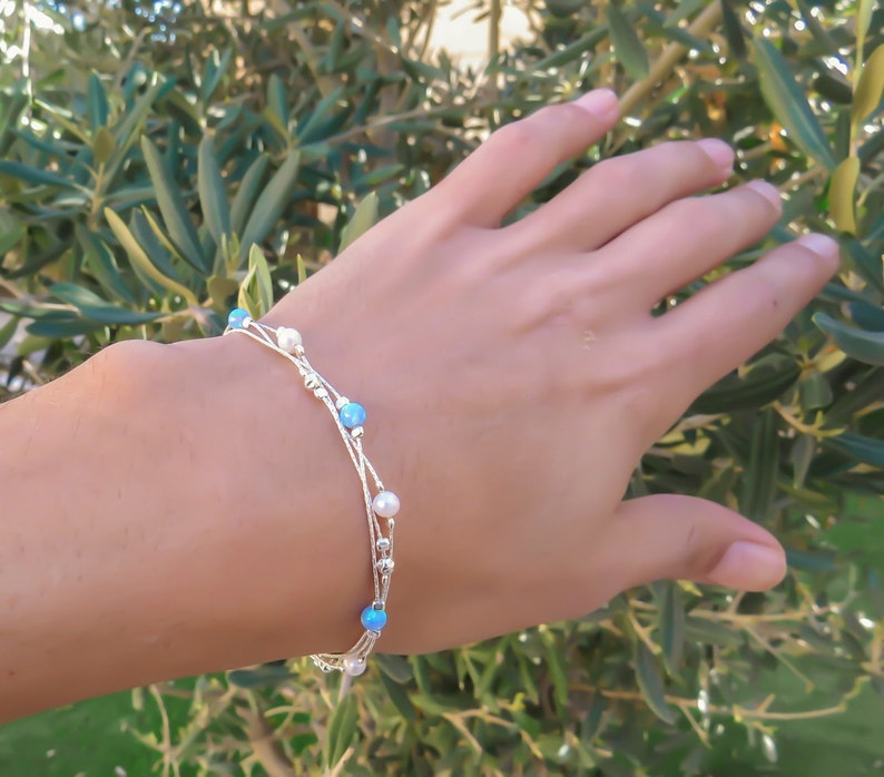 K&ouml;nnte beinhalten: Ein silbernes Armband mit mehreren Kettenstr&auml;ngen und kleinen blauen und wei&szlig;en Perlen.