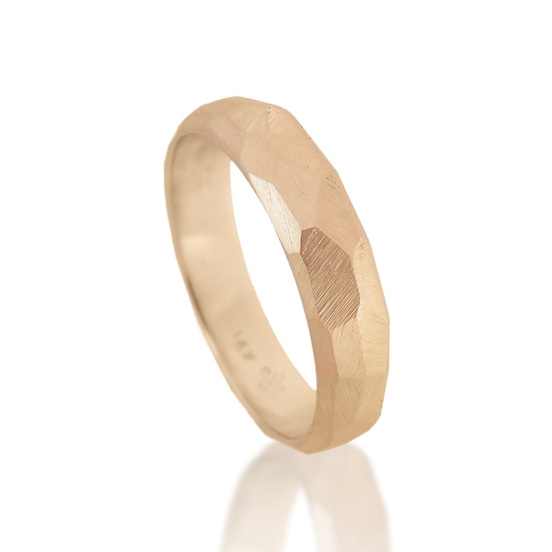 May include: A gold band ring with a faceted, geometric design. The ring is made of a smooth, polished metal.