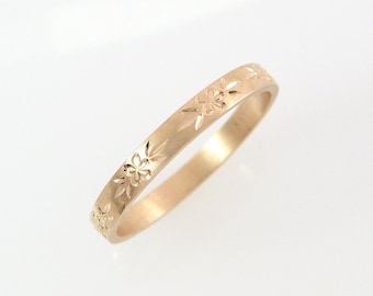 May include: A thin gold band ring with a delicate floral design engraved around the entire band.