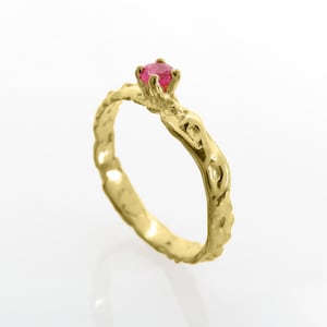 Può includere: Un anello d'oro con una fascia testurizzata e una piccola pietra preziosa rotonda rosa.
