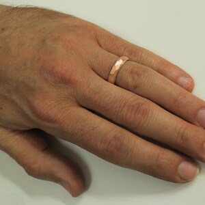 May include: A hammered gold wedding band on a finger.