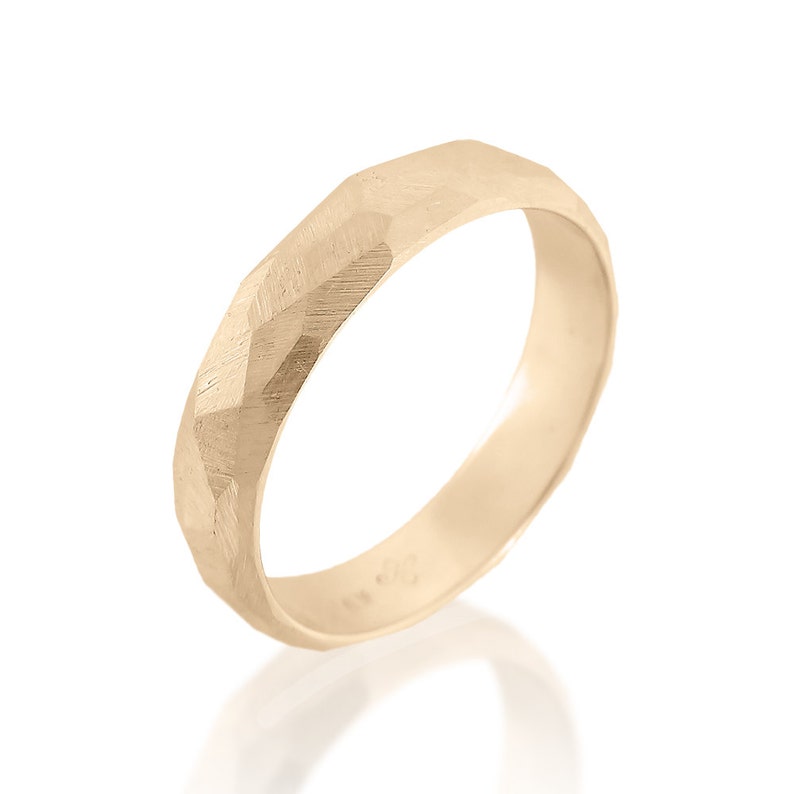 May include: A gold band ring with a textured, faceted design. The ring is made of a smooth, polished metal.
