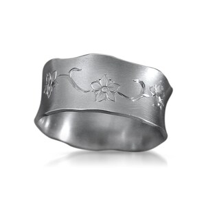 Puede incluir: Anillo de servilleta de plata con un dise&ntilde;o floral. El anillo es ondulado y tiene un acabado cepillado.