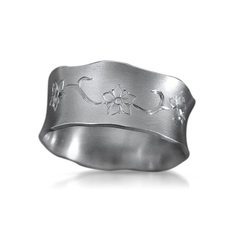 Puede incluir: Anillo de servilleta de plata con un dise&ntilde;o floral. El anillo es ondulado y tiene un acabado cepillado.