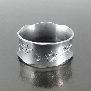 Puede incluir: Un anillo de plata con un borde ondulado y un dise&ntilde;o floral grabado.