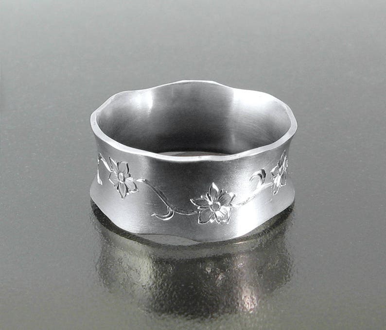 Puede incluir: Un anillo de plata con un borde ondulado y un dise&ntilde;o floral grabado.