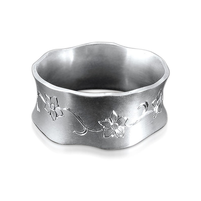 Puede incluir: Un anillo de plata con una banda ondulada y un dise&ntilde;o floral grabado. Las flores son estilizadas y tienen cinco p&eacute;talos.