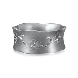 Puede incluir: Un anillo de plata con una banda ondulada y un dise&ntilde;o floral grabado. El dise&ntilde;o presenta flores y enredaderas delicadas.