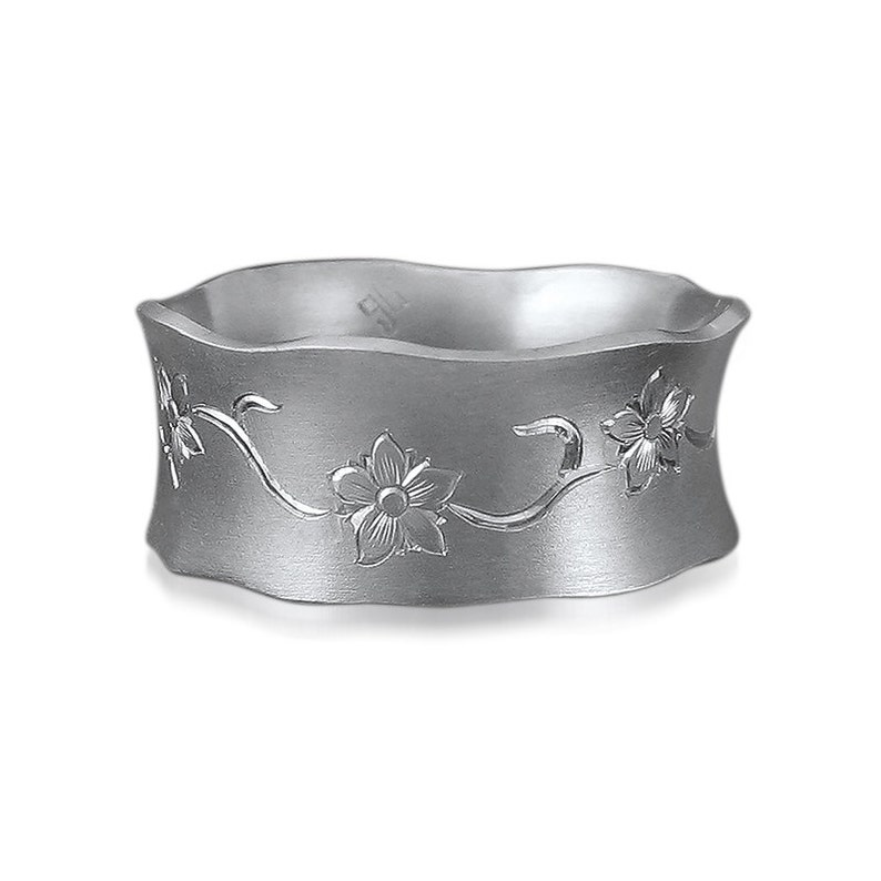 Puede incluir: Un anillo de plata con una banda ondulada y un dise&ntilde;o floral grabado. El dise&ntilde;o presenta flores y enredaderas delicadas.