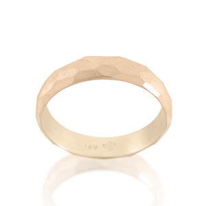 May include: A gold band ring with a textured, faceted surface. The ring is made of 14k gold.