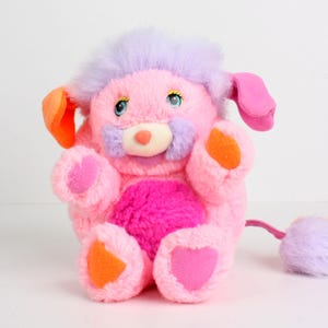 Peut inclure: Une peluche vintage aux tons rose, violet et orange. Le jouet a une tête violette duveteuse, un corps rose et des accents orange sur les oreilles et les pattes. Il présente des yeux bleus, un nez rose et une queue duveteuse.