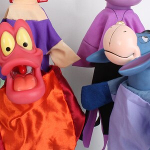 Puede incluir: Una colecci&oacute;n de marionetas coloridas. Una marioneta tiene una boca grande y abierta con ojos amarillos y una lengua roja. Otra es un burro azul con una expresi&oacute;n triste. Las marionetas est&aacute;n vestidas con telas de varios colores, incluyendo rojo, naranja, morado y azul.