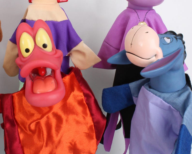 Puede incluir: Una colecci&oacute;n de marionetas coloridas. Una marioneta tiene una boca grande y abierta con ojos amarillos y una lengua roja. Otra es un burro azul con una expresi&oacute;n triste. Las marionetas est&aacute;n vestidas con telas de varios colores, incluyendo rojo, naranja, morado y azul.