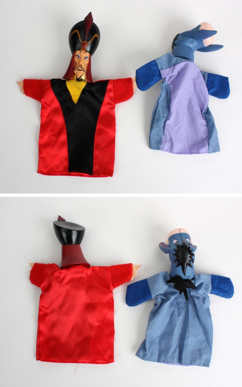 Puede incluir: Dos marionetas de mano con personajes de dibujos animados. Una marioneta tiene un atuendo rojo y negro con un sombrero negro. La otra marioneta es azul y morada. Las marionetas est&aacute;n sobre un fondo blanco.
