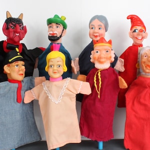 May include: A collection of vintage hand puppets featuring various characters. The puppets have painted faces and are dressed in colorful fabric costumes. Characters include a devil, a king, and an old woman. The puppets are mounted on blue sticks.