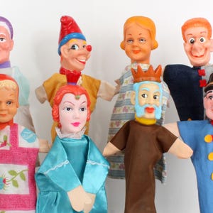 May include: A collection of vintage hand puppets with painted faces and fabric costumes. The puppets include a clown, a queen, a king, and other characters, all with detailed facial features and colorful outfits. The puppets are arranged against a plain white background.