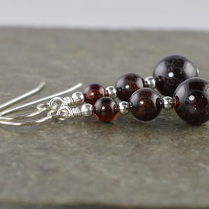 Op de afbeelding: Een paar zilveren oorhangers met rode granaatstenen. De oorbellen hebben een eenvoudig ontwerp met drie ronde granaatstenen aan elke oorbel.