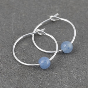 May include: Silver hoop earrings with a light blue gemstone bead on each hoop.