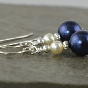 May include: A pair of silver dangle earrings with a dark blue pearl and two cream-coloured pearls.