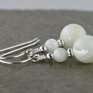 May include: White pearl earrings with silver hooks and beads. The pearls are round and have a slight iridescent sheen.