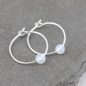 May include: A pair of silver hoop earrings with a white opal bead on each hoop.