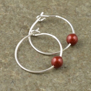 May include: Silver hoop earrings with a small, round, red bead on each hoop.