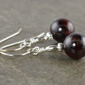 May include: A pair of silver earrings with dark red gemstone beads. The earrings have a simple design with a small silver bead connecting the gemstone to the hook.