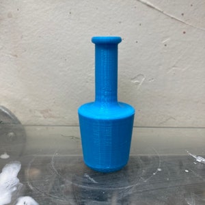 May include: A light blue plastic bottle stopper with a narrow neck and a wider base.