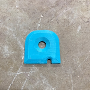 May include: A light blue plastic object with a round hole in the center and a small cutout on the side. The object is shaped like a rounded rectangle.