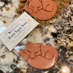 May include: A terracotta-colored ceramic fox figurine in the shape of a sleeping fox. The figurine is packaged in a clear plastic bag with a white label that reads "Brown Sugar Saver keep your brown sugar soft" and a website address.