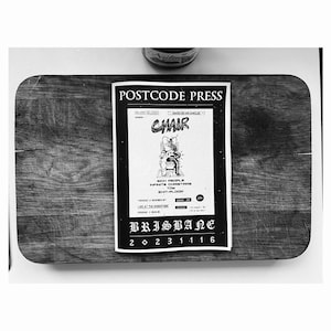 May include: Black and white image of a flyer for "CHAIR" by Postcode Press. The flyer features an illustration of a person in an electric chair. Text includes "Sick People, Infinite Christmas, Tom, Exit-Ploom", and "Brisbane 20231116".