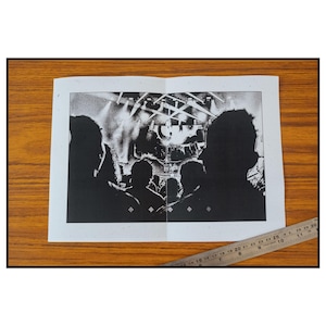 May include: Black and white photo of a concert crowd, with the stage and band out of focus in the background.