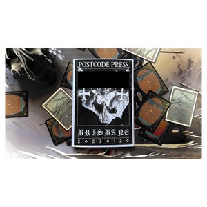 May include: Black and white magazine cover with the text "POSTCODE PRESS" and "BRISBANE 20230120". The cover features a black and white illustration of a person in a hooded cloak standing in front of a cross.