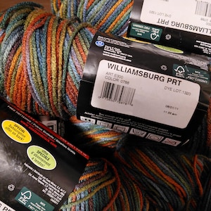 May include: Close-up of several skeins of Williamsburg PRT yarn. The yarn is a mix of colors including orange, blue, green, and brown. The labels show the color code 0788 and the dye lot 1320. The yarn is suitable for knitting and crochet projects.