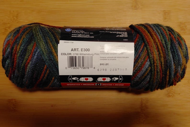 May include: A skein of Red Heart yarn in the Williamsburg Print colorway. The yarn is a blend of blue, green, and orange hues. The label displays the product details, including the art number E300 and color code 0788.