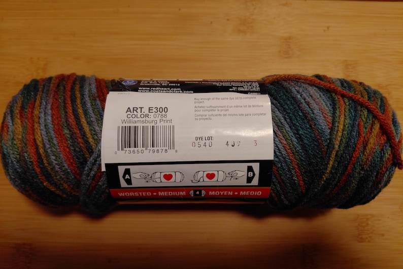May include: A skein of Williamsburg Print yarn, featuring a blend of colors including teal, orange, and gold. The label displays the product details: ART. E300, COLOR: 0788, and WORSTED - MEDIUM. Ideal for knitting and crochet projects.