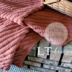 May include: A close-up of a knitted blanket in a rust colour. The blanket is folded and draped over a brick surface. The text "Knitting Pattern" is visible in a circle on the blanket. The text "LT designs" is visible on the brick surface.