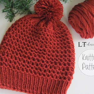 May include: A red knitted hat with a pom pom on top. The hat is made with a textured stitch and has a simple, classic design. The yarn is also pictured next to the hat.