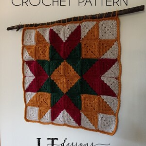 May include: A crochet wall hanging with a starburst pattern in shades of red, green, yellow, and white. The hanging is attached to a branch with twine. The text "LT designs" is visible at the bottom of the image.